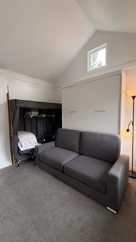 Vaulted ceiling featuring a triangular window, built-in sliding panel storage, and plush gray carpeting