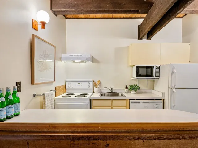 Kitchen featuring under cabinet range hood, white appliances, a sink, light countertops, and beam ceiling