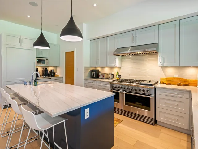 Kitchen featuring light stone counters, stainless steel appliances, a breakfast bar, pendant lighting, and under cabinet range hood