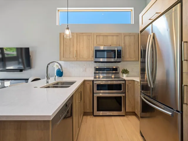 Kitchen with appliances with stainless steel finishes, a peninsula, tasteful backsplash, light stone counters, and decorative light fixtures