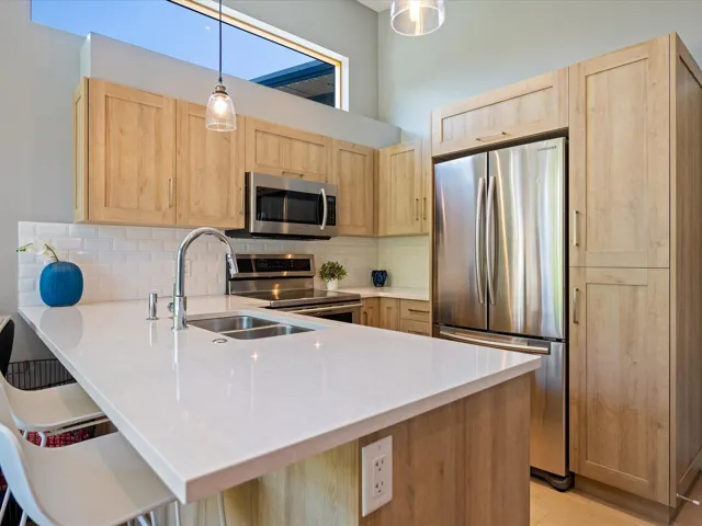Kitchen featuring light brown cabinetry, appliances with stainless steel finishes, decorative light fixtures, and backsplash