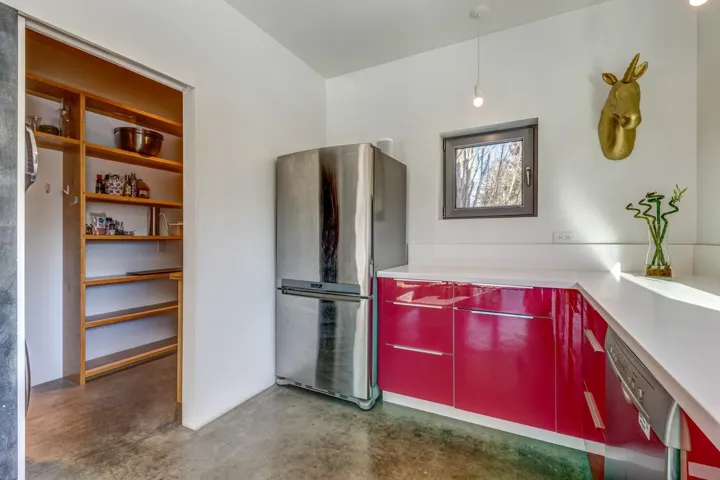 Kitchen with appliances with stainless steel finishes, concrete flooring, light countertops, red cabinetry, and modern cabinets