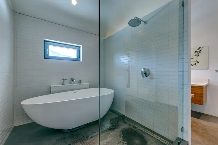 Bathroom featuring a walk in shower, a freestanding bath, vanity, tile walls, and concrete flooring