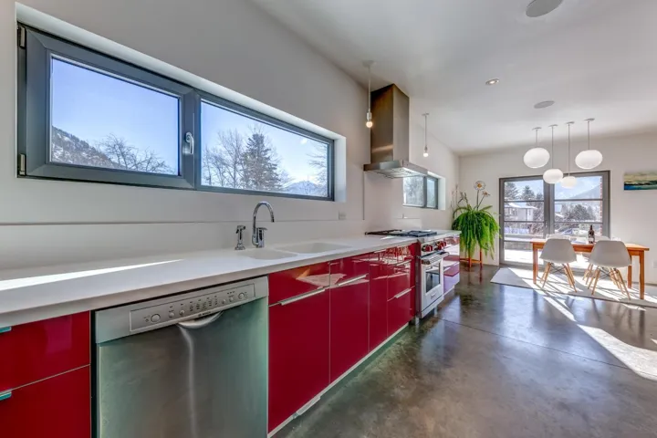 Kitchen with red cabinetry, stainless steel appliances, concrete floors, wall chimney exhaust hood, and pendant lighting