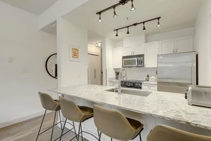 Kitchen featuring white cabinetry, light stone countertops, stainless steel appliances, a breakfast bar area, and rail lighting