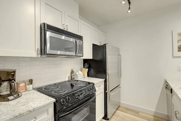 Kitchen with stainless steel appliances, white cabinetry, tasteful backsplash, light stone countertops, and light wood-style floors