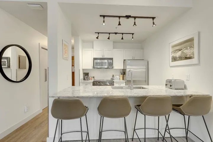 Kitchen with a peninsula, a breakfast bar area, white cabinetry, backsplash, and light stone countertops
