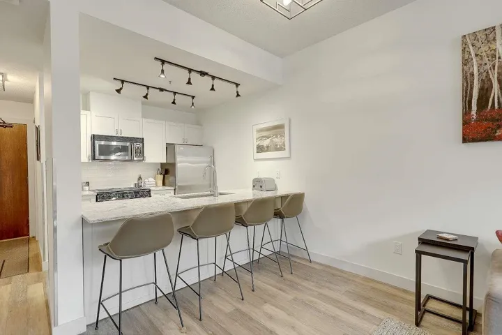 Kitchen featuring a kitchen breakfast bar, white cabinets, a peninsula, light wood finished floors, and light stone countertops