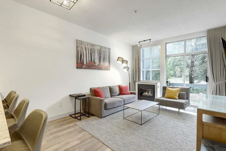 Living room featuring a textured ceiling, light wood-style flooring, a glass covered fireplace, and rail lighting