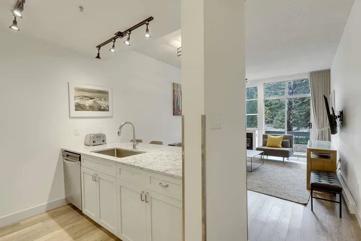 Bar area with track lighting, a glass covered fireplace, light stone countertops, light wood-style floors, and white cabinetry