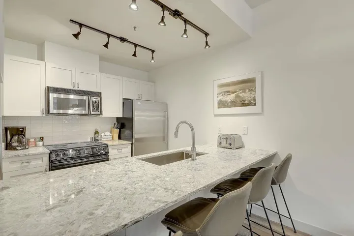 Kitchen with a breakfast bar area, white cabinetry, light stone counters, a peninsula, and stainless steel appliances
