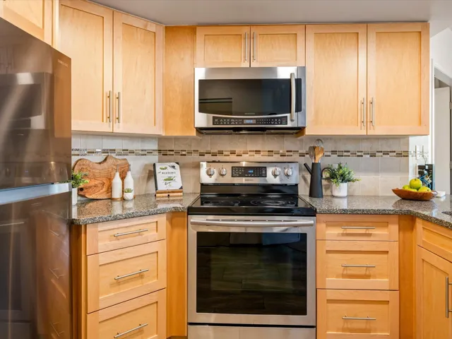 Kitchen featuring light brown cabinetry, stainless steel appliances, and dark stone counters