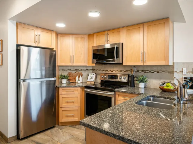 Kitchen with stainless steel appliances, dark stone countertops, light brown cabinets, and backsplash