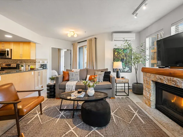 Living area with light carpet, a stone fireplace, a wall unit AC, and track lighting