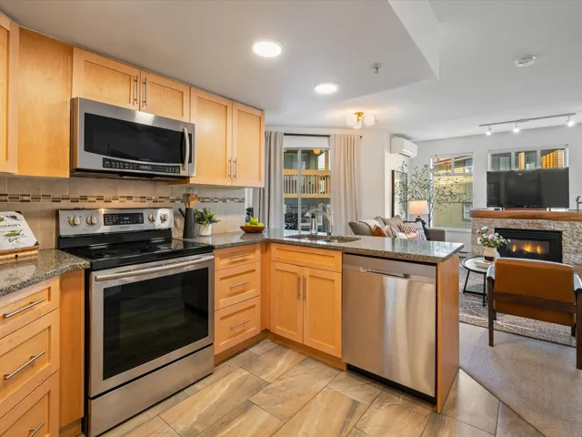 Kitchen with stainless steel appliances, a peninsula, light brown cabinets, dark stone counters, and open floor plan