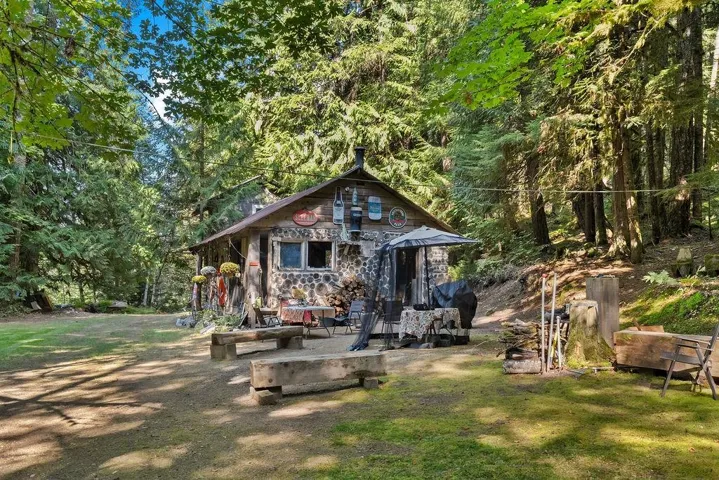 View of front of house featuring a forest view, a front lawn, and stone siding