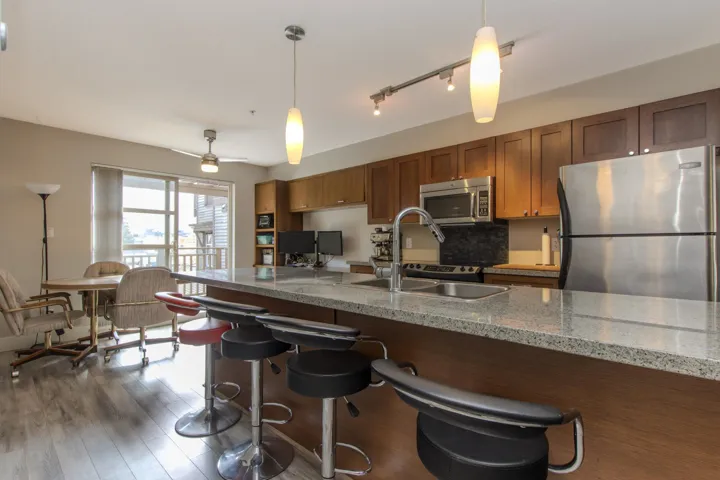 Kitchen with appliances with stainless steel finishes, decorative light fixtures, a breakfast bar area, brown cabinetry, and light stone counters