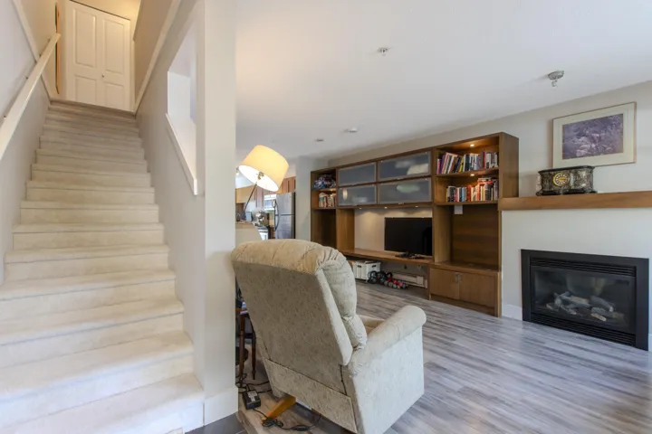 Living room with stairs, light wood-style flooring, and a glass covered fireplace