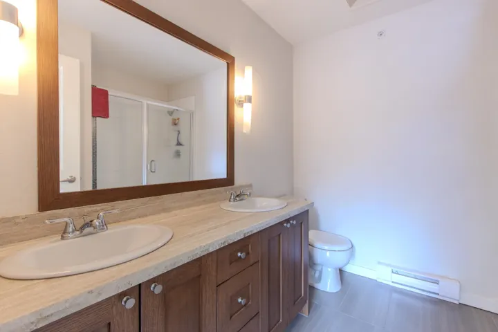Full bath featuring baseboard heating, double vanity, a shower stall, and dark tile patterned flooring
