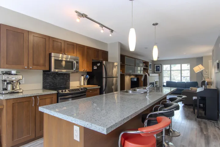 Kitchen with open floor plan, stainless steel appliances, light stone countertops, pendant lighting, and a kitchen island with sink
