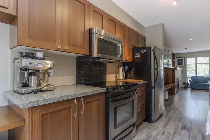 Kitchen featuring stainless steel electric range, tasteful backsplash, brown cabinets, light stone countertops, and light wood finished floors