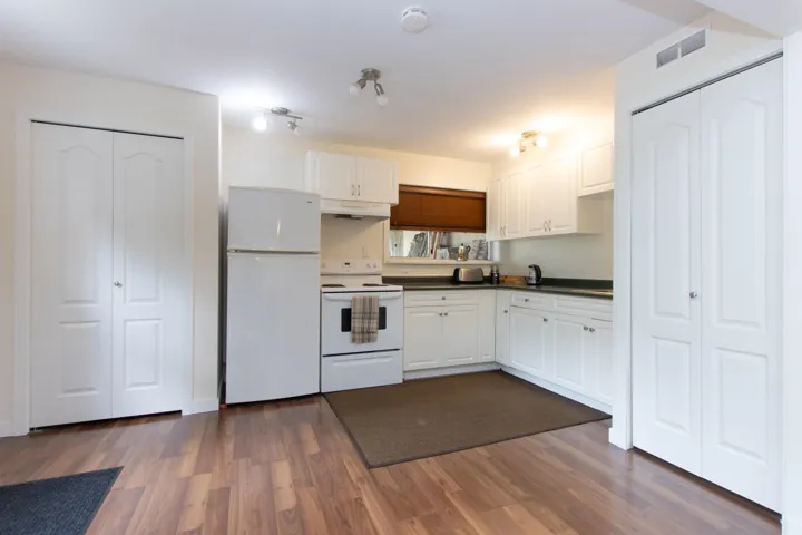 Kitchen with white appliances, under cabinet range hood, dark countertops, and dark wood finished floors