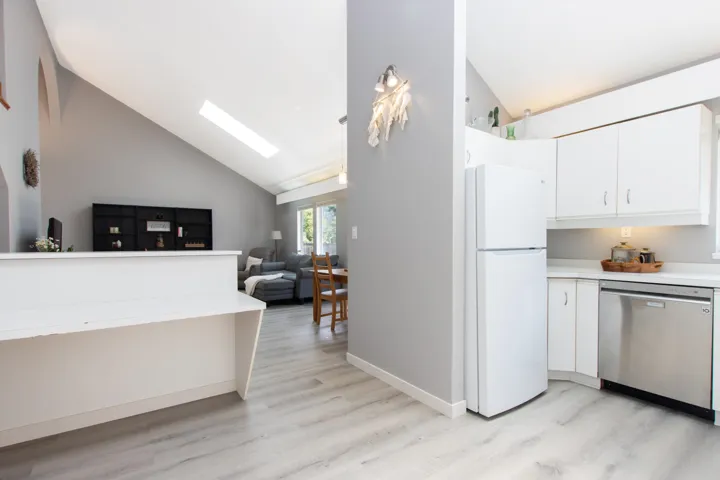 Kitchen featuring stainless steel dishwasher, freestanding refrigerator, a skylight, high vaulted ceiling, and light wood-type flooring