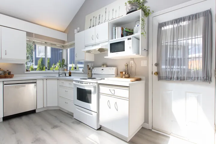 Kitchen featuring white appliances, under cabinet range hood, lofted ceiling, light wood finished floors, and white cabinets