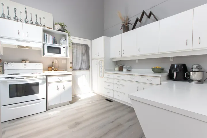 Kitchen featuring white appliances, light countertops, under cabinet range hood, light wood-style flooring, and white cabinetry