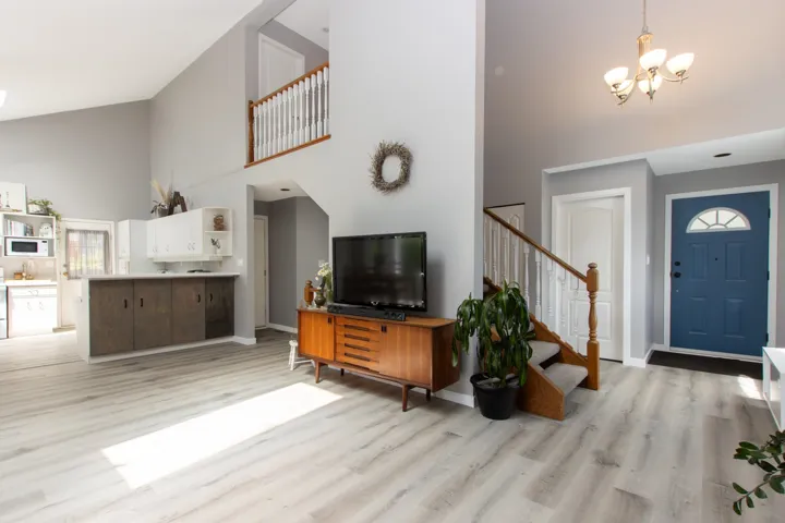 Entryway with high vaulted ceiling, light wood finished floors, stairway, and a chandelier