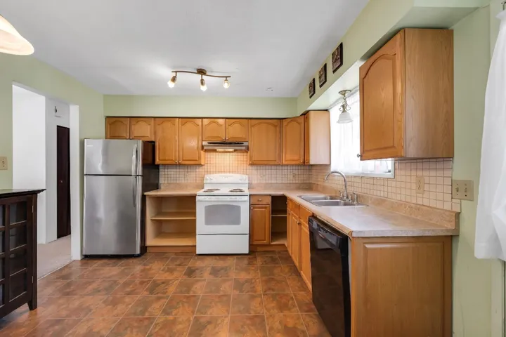 Well-appointed kitchen featuring wood cabinetry, stainless steel refrigerator, white electric range with overhead microwave, and a double basin stainless steel sink