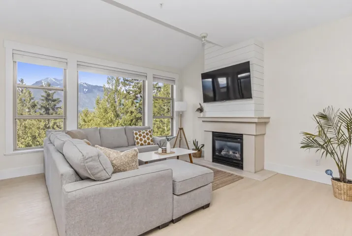 Living area featuring large windows, light wood-finish flooring, a contemporary fireplace with a stone mantel, a shiplap accent wall, and a ceiling fan