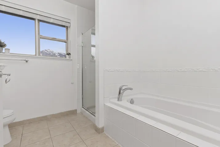 Full bathroom featuring an inset bathtub with white tile surround, a separate glass-enclosed shower, and a large window with mountain scenery