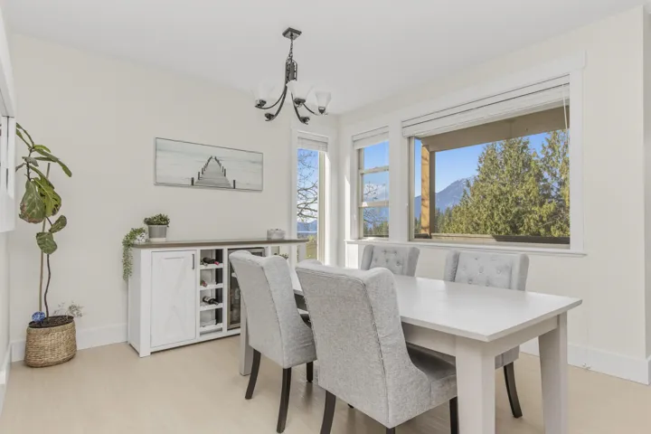Spacious dining area featuring expansive windows with mountain and tree scenery, light wood-finish flooring, a contemporary chandelier, and a built-in beverage cooler with wine storage