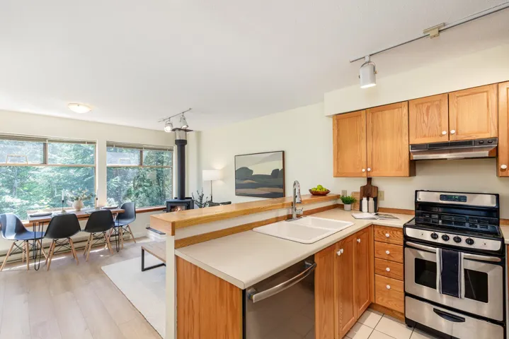 Open-concept kitchen featuring light wood cabinetry, stainless steel appliances, and a double basin sink