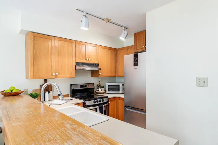 Kitchen featuring light wood cabinetry, stainless steel appliances, a double basin sink, track lighting, and a breakfast bar with a wood-finish surface