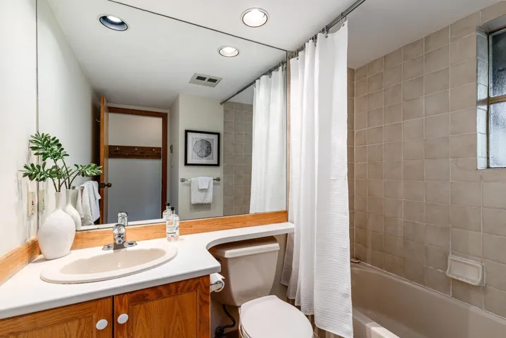 Bathroom featuring a wood-finish vanity with a built-in sink, a full-width wall mirror, recessed lighting, and a tiled shower/tub combination