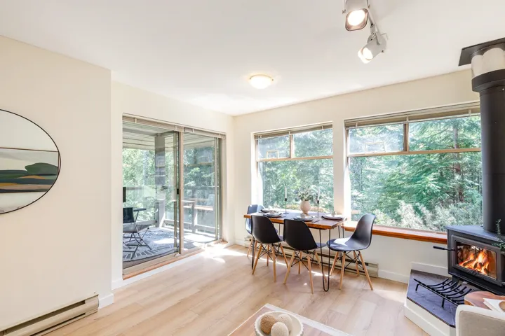 Living area featuring a wood-burning stove, wood-finish flooring, floor-to-ceiling windows, and sliding glass doors opening to an outdoor deck