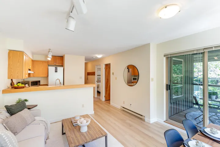 Open-concept living area featuring light wood-finish flooring, a kitchen with natural wood cabinetry and a breakfast bar, and a sliding glass door providing exterior access