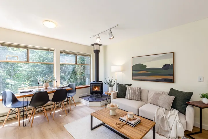Living area featuring a freestanding wood stove with a corner hearth, large windows, and light wood-finish flooring