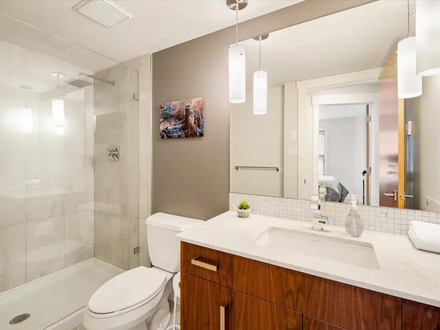 Ensuite bathroom featuring vanity, tasteful backsplash, a tile shower, toilet, and visible vents