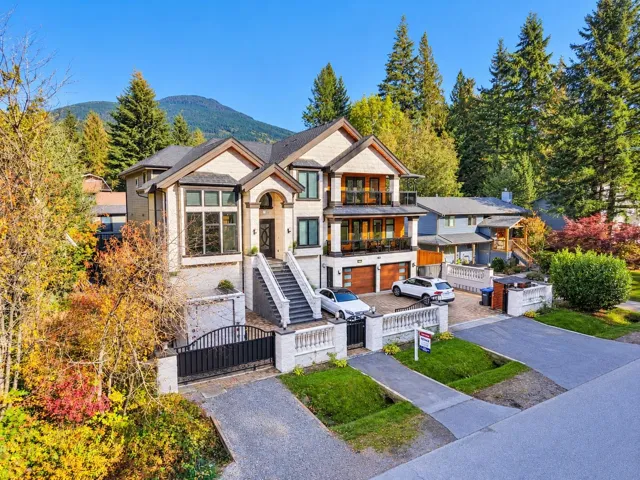 Multi-level exterior featuring light-toned masonry, tiered balconies with glass railings, an elevated concrete staircase, integrated wood-finish garage doors, and a mountain backdrop