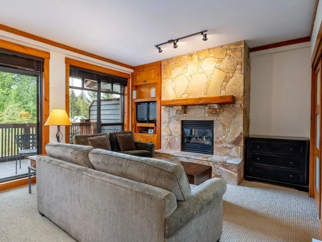 Carpeted living room featuring a stone fireplace, built in features, track lighting, and ornamental molding