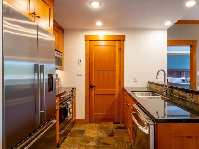 Kitchen featuring appliances with stainless steel finishes, brown cabinets, dark stone countertops, recessed lighting, and a peninsula