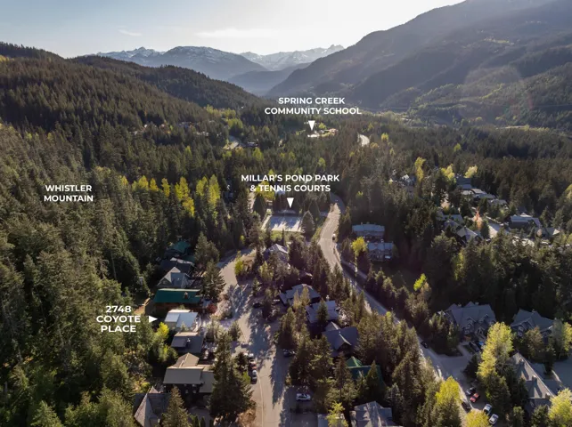 Aerial view of a residential area surrounded by dense forest and mountains, featuring nearby community amenities and a prominent mountain range