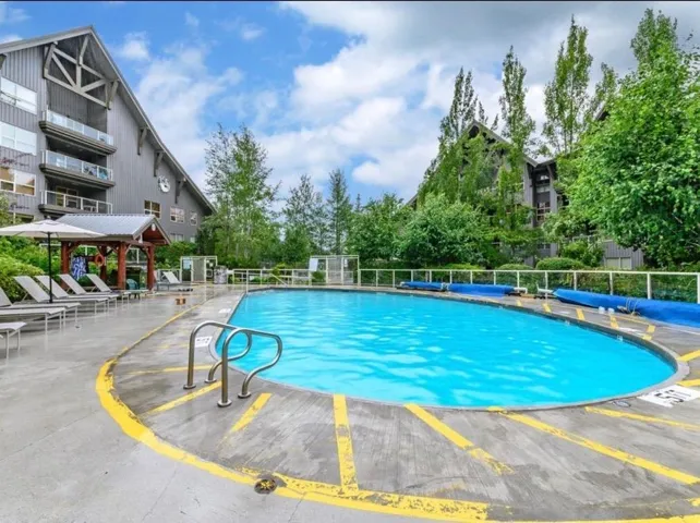 Outdoor swimming pool with concrete surround, bordered by a glass panel fence