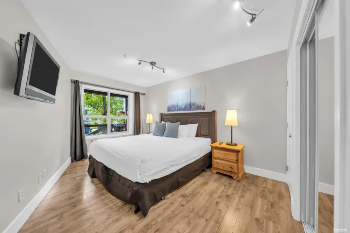 Bedroom featuring wood-finish flooring, a double window, track lighting, and a mirrored sliding closet door
