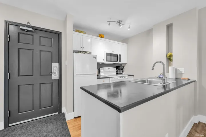 Compact kitchen area featuring white cabinetry, a stainless steel sink, dark countertops, and integrated appliances