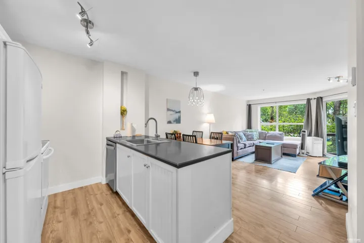 Open-concept living area with wood-finish flooring, a kitchen island featuring a double-basin sink, and recessed shelving