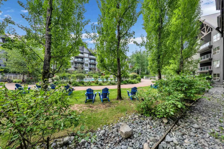 Expansive outdoor common area featuring a manicured lawn, established trees, and river rock landscaping